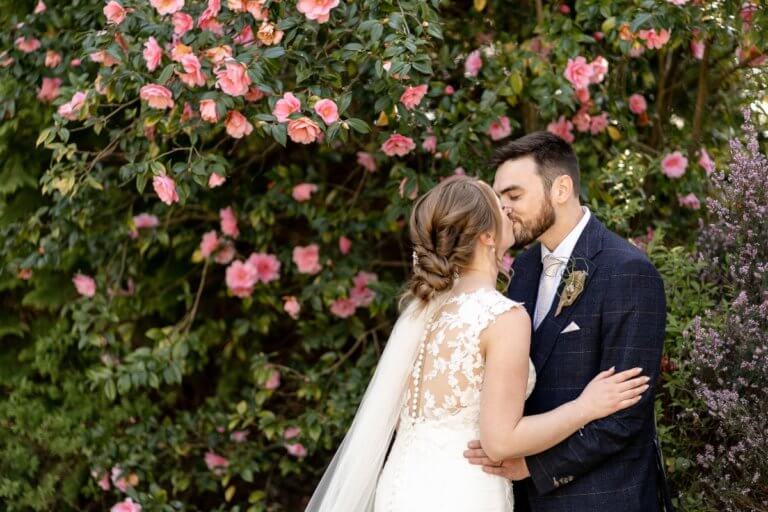 The bride and groom share a kiss in front of the rose bush in the garden