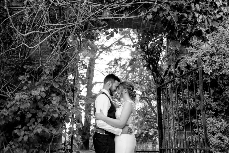 The bride and groom embrace in the garden archway