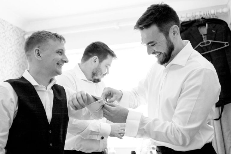 The groom helps a groomsman with his cufflinks