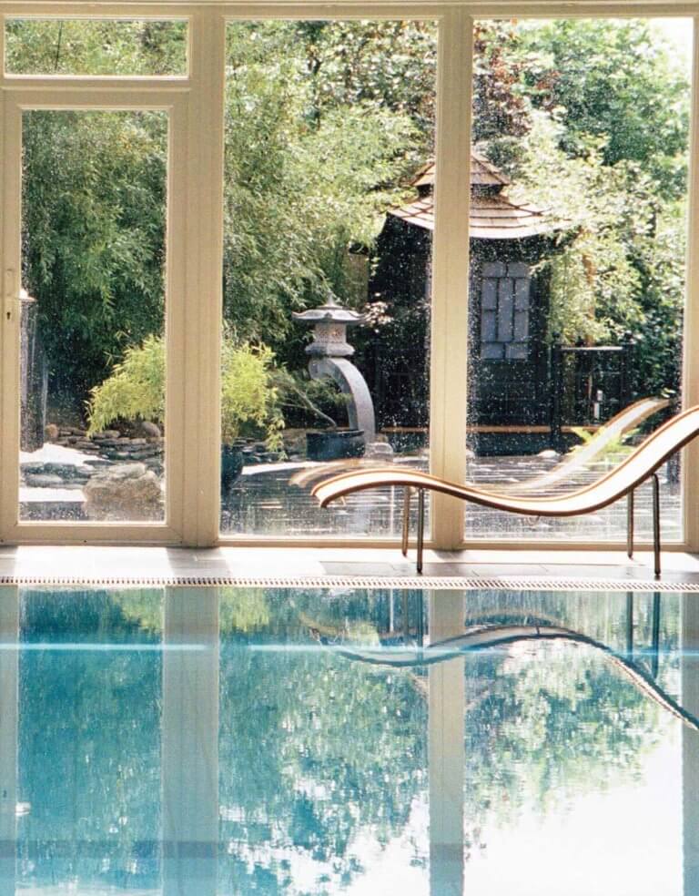 Swimming pool on bright day with large windows looking out to garden