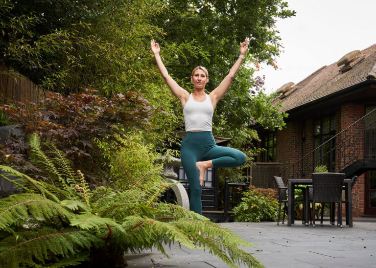 Woman stands in Thai-inspired garden in yoga pose 'tree pose'