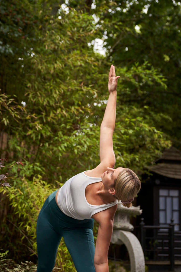 Woman in Zen Garden courtyard garden stands in triangle pose yoga position