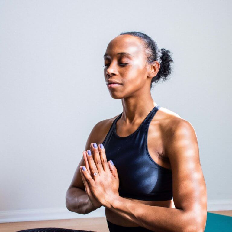 Woman sits on yoga mat with palms together and eyes closed, meditating