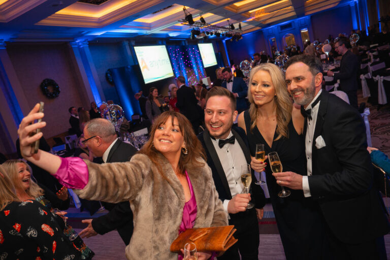 Team members dressed in black tie take a selfie at awards ceremony