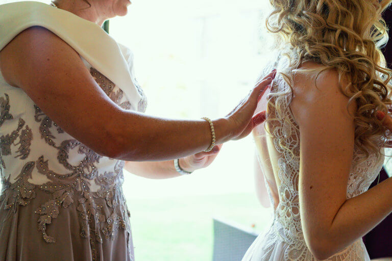 Mother of the Bride fastens the back of the Brides bridal gown