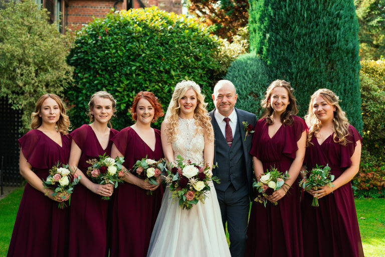 The bride along with her father and bridesmaids pose for a group shot in the garden