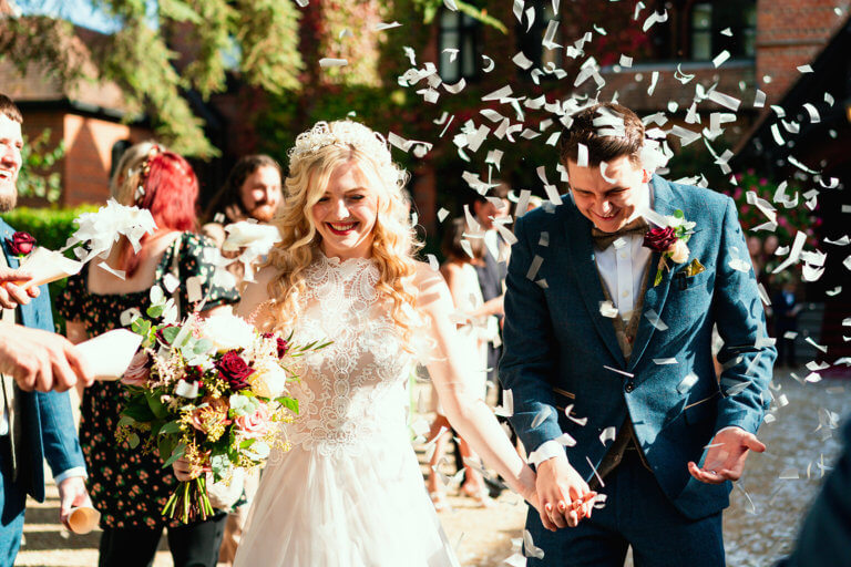 The Bride and Groom smile whilst confetti is thrown