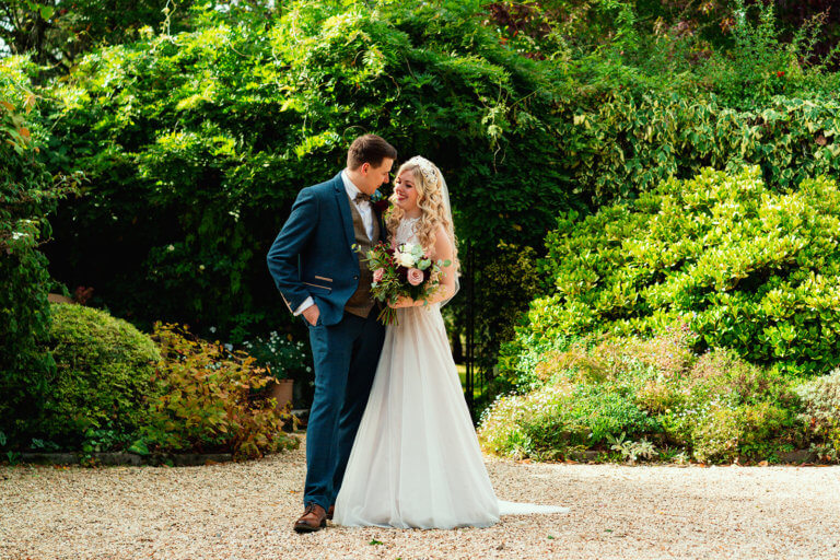 Bride and Groom pose in the garden, smiling at her