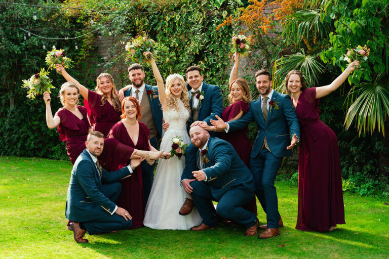 The bride, groom and wedding party raise their arms in the air and smile