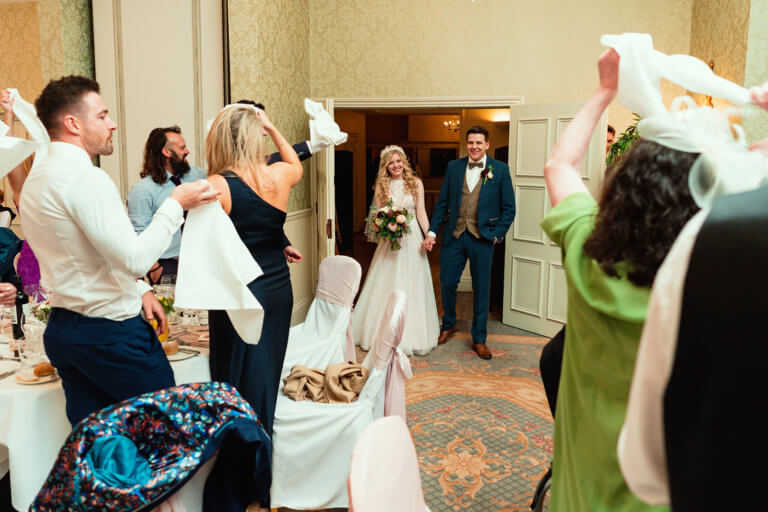 Guests welcome the married couple into the wedding breakfast by waving their napkins