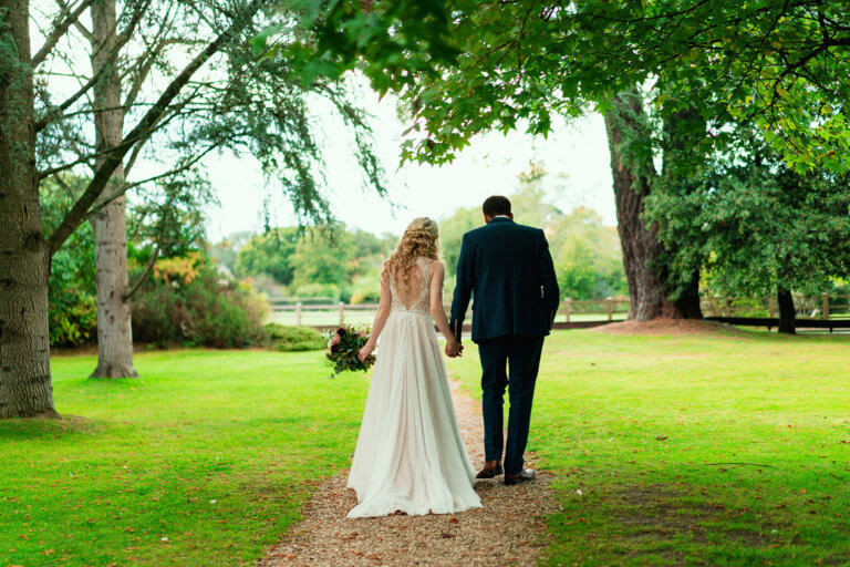 The couple walk away from the camera, through the garden, hand in hand