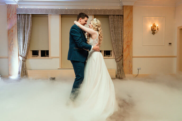 The bride and groom dance together on a smoky dance floor