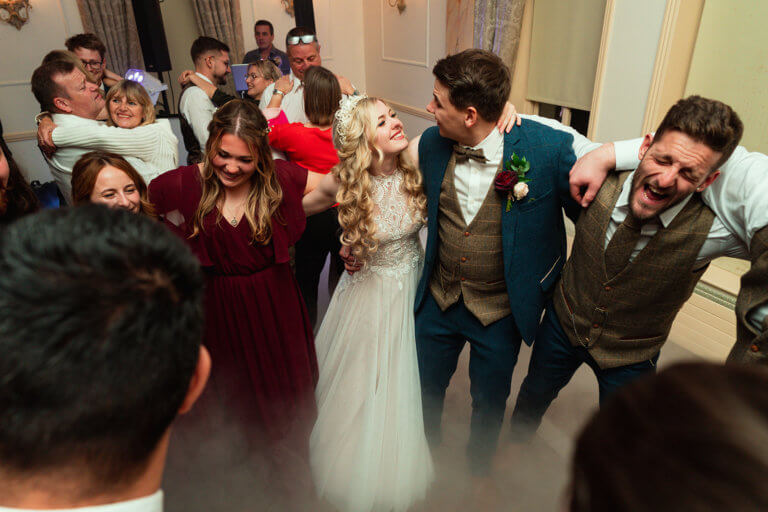 Bride and groom dance with guests on the dancefloor with smoke machine on