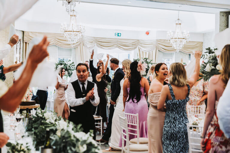 Wedding guests cheer as the bride and groom enter the wedding breakfast