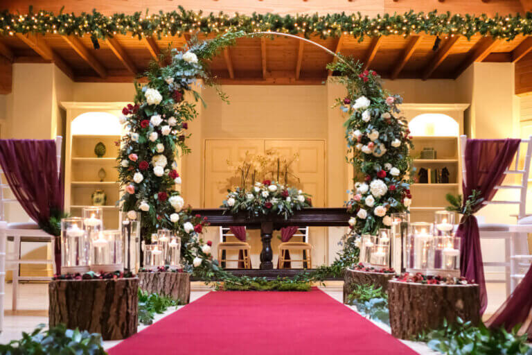 Wedding arch with flowers set up in hotel lounge for wedding ceremony with red aisle runner and candles either side of the aisle