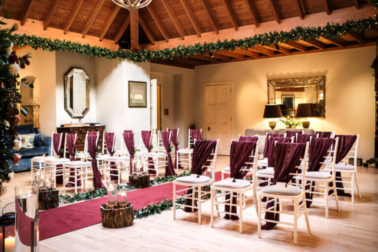 The Lounge set for a wedding ceremony with burgundy sashes on wooden chairs