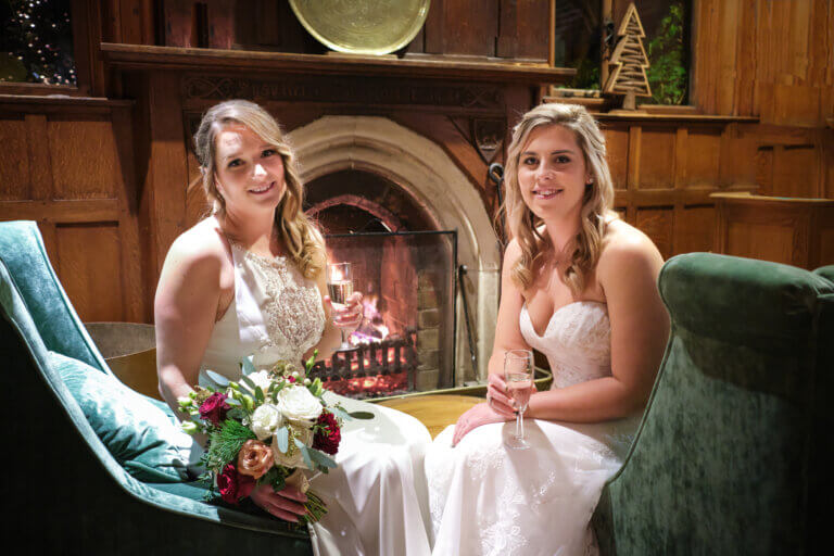 Hannah & Steph in front of the roaring fire with a glass of champagne
