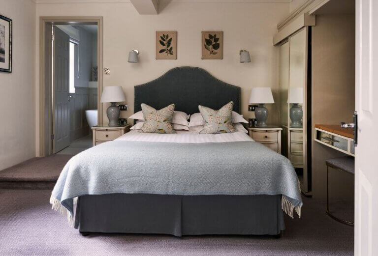 A freshly made bed in a suite at Careys Manor with a duck-egg blue throw, crisp white sheets and floral cushions