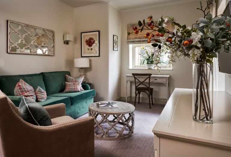 The lounge are ain a suite at Careys Manor with a green velvet sofa, white walls, a drum shaped coffee table and a vase of flowers