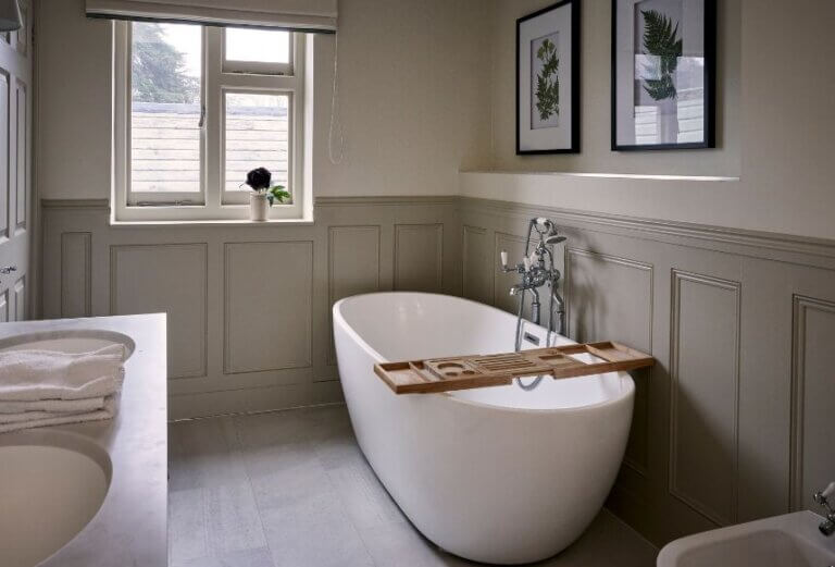 A large paneled bathroom with an over-sized white bath tub with traditional mixer taps and shower head.