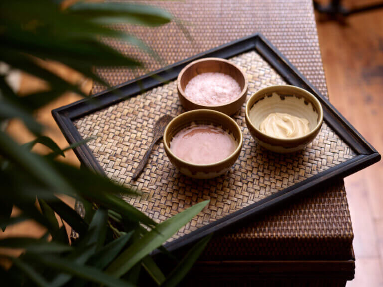 Three dishes of skincare pots displayed in a triangle formation on a bamboo tray.
