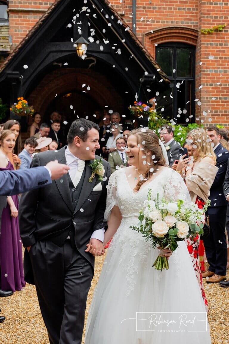 Bride and groom leaving wedding ceremony surrounded by guests throwing confetti at Careys Manor Hotel & SenSpa wedding venue in The New Forest