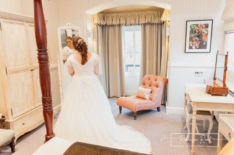 Bride admires her wedding dress through mirror in bedroom at Careys Manor Hotel & SenSpa wedding venue in The New Forest