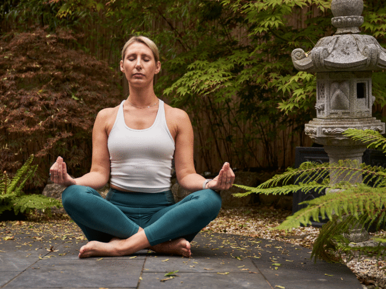 Woman sits crossed-legged and meditating in the Zen Garden courtyard at Careys Manor Hotel & SenSpa