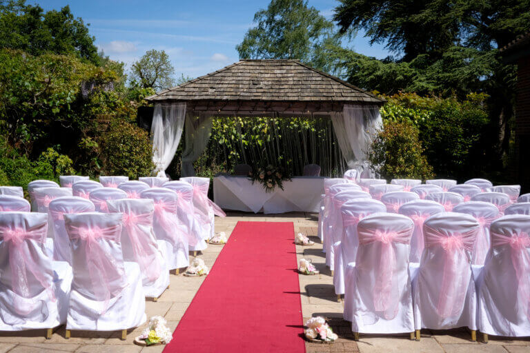 Cedar Garden set ready for an outdoor wedding ceremony with white chair covers and a red carpet leading to the wooden gazebo.