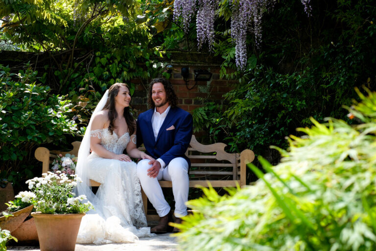 Bride and Groom sat on a bench surrounded by wisteria