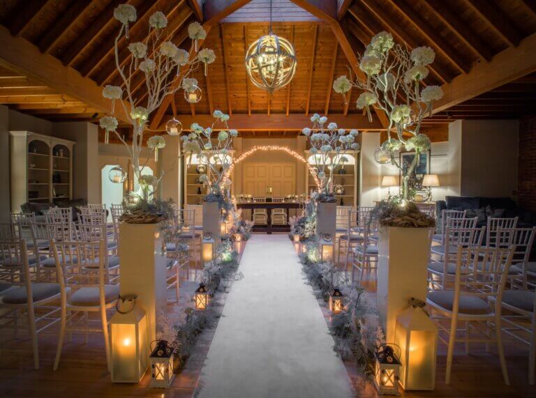 Beautiful winter wedding ceremony at Careys Manor Hotel's Lounge, with candles lighting up the aisle and white floral displays
