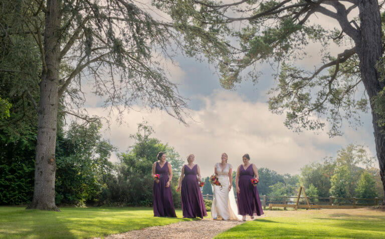 Bride walks up path with bridesmaids all smiling in grounds of Careys Manor Hotel in the New Forest