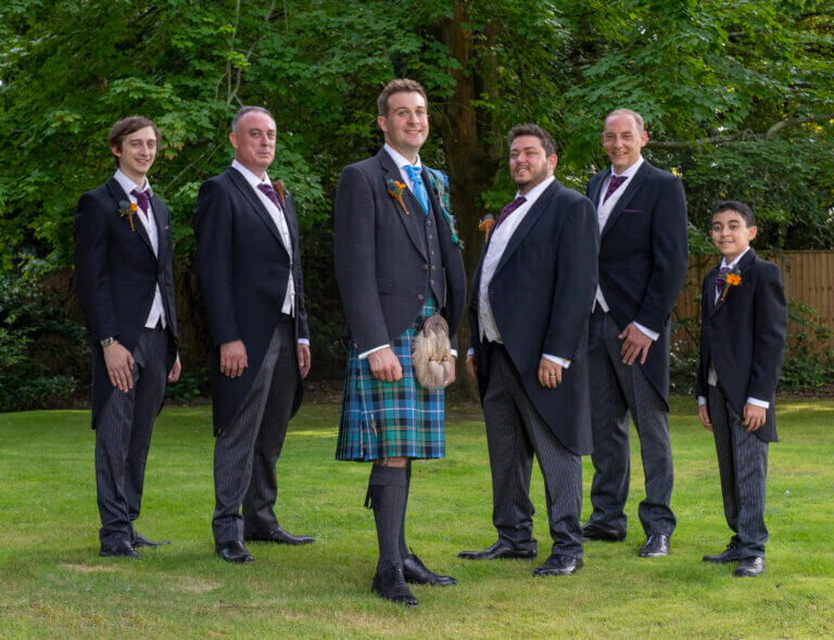 Groom poses with groomsmen for photo in grounds of Careys Manor Hotel with leafy green backdrop