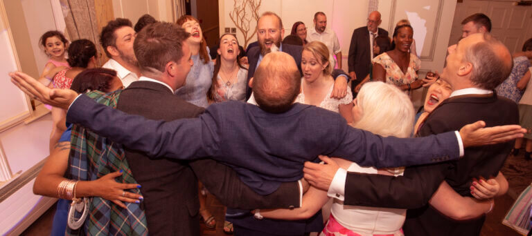 Wedding guests huddled in a circle on the dancefloor singing