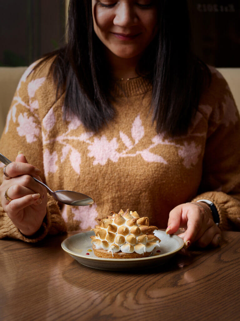 Woman takes spoon to meringue dessert on wooden table in Cambium restaurant, Brockenhurst