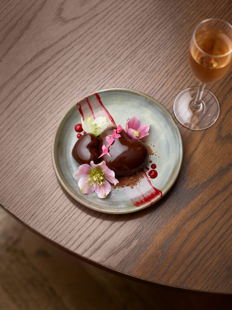 Heart shaped chocolate glazed dessert and glass of pink champagne on wooden table in Cambium restaurant, Brockenhurst for Valentine's Day