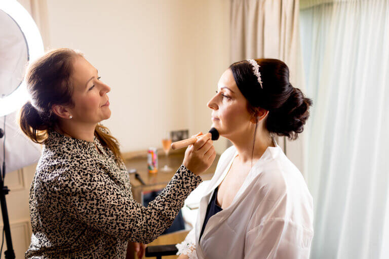 Bride getting makeup professionally done on wedding day at Careys Manor hotel