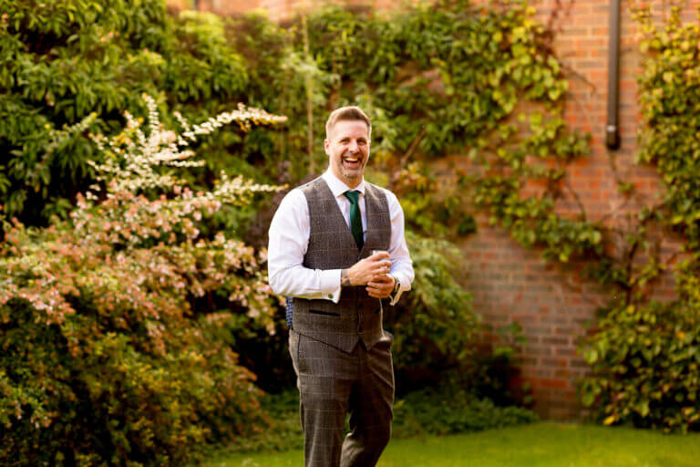 Groom smiles happily on wedding day in Careys Manor gardens surrounded by green and orange autumn trees