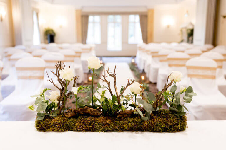 Wedding ceremony set up at Careys Manor Hotel with white chairs and forest-inspired floral display