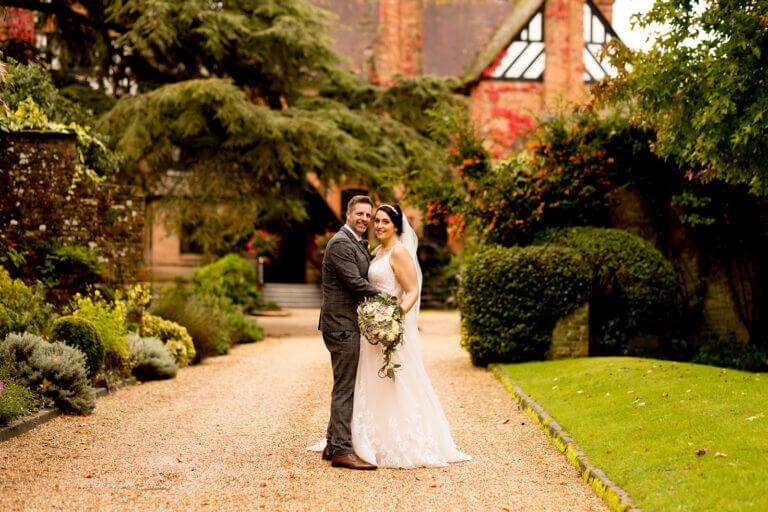 Bride and groom on wedding day kissing in grounds of Careys Manor hotel with manor house in background surrounded by green trees