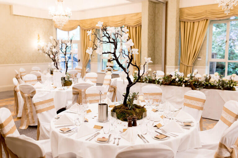Tables set for wedding breakfast at Careys Manor hotel with white tablecloths and white floral centrepieces