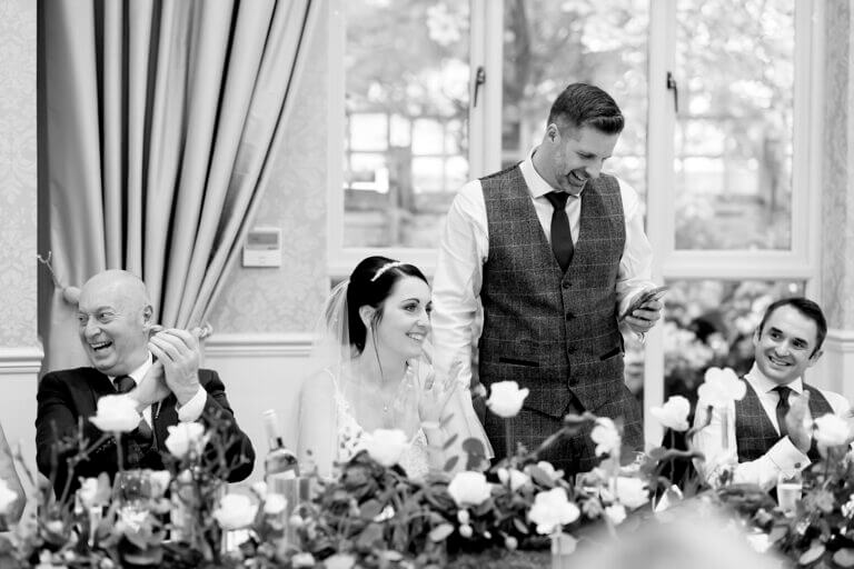 Bride and groom on head table on wedding day with groom standing to give speech at Careys Manor hotel