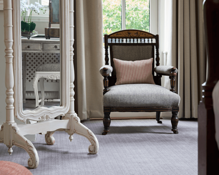 A freestanding mirror and wooden armchair with grey patterned upholstery and red and cream striped cushion in luxury hotel suite in Careys Manor Hotel & SenSpa