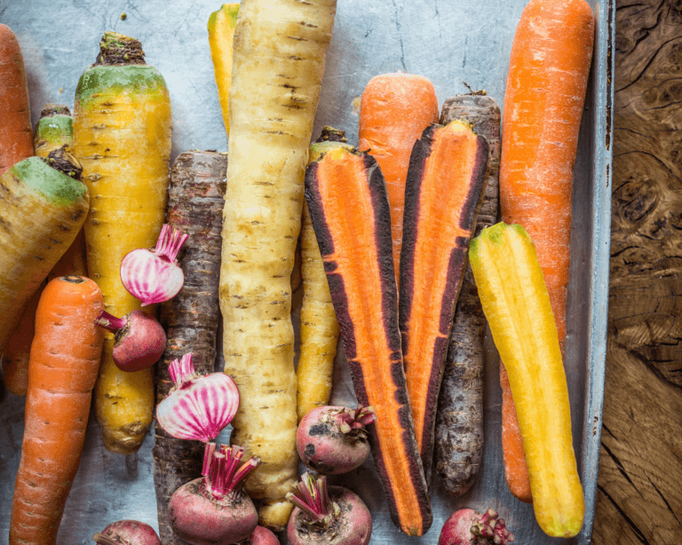 Fresh pick of coloured carrots, parsnips on a roasting tray on wooden table