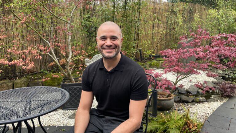 SenSpa Spa Operations Manager, Jermaine Lee, sits outside in Zen Garden courtyard smiling