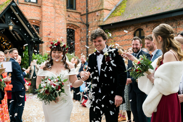 The bride and groom smile as guests throw confetti at the front of the hotel at Hampshire wedding venue Careys Manor Hotel & SenSpa.