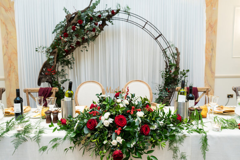 Top table with red floral arrangement and moon arch behind the table